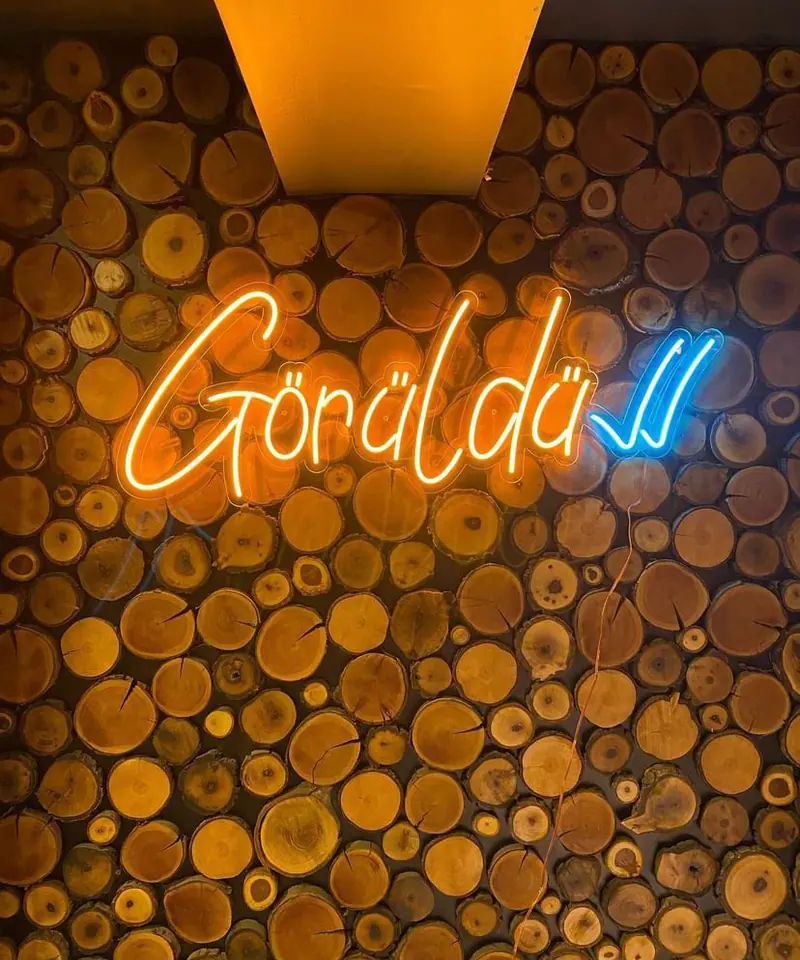 Kütük kaplı iç mekân duvarında turuncu LED neon-flex yazı ve mavi çift tik işareti